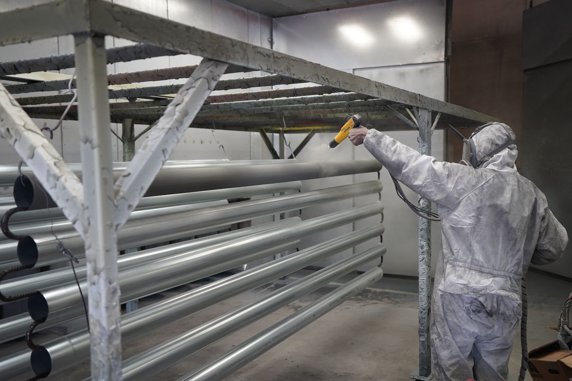 Technician applying powder coating to metal pipes in a workshop setting.
